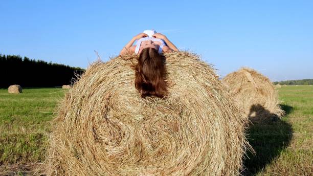 young female lies on a haystack and throws his hat. Rural area. freedom concept