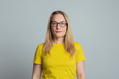 Attractive woman in glasses, looking positive, wearing casual yellow t shirt, gray background