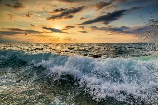 A Wave Is Breaking And Splashing As The Sun Sets On the Ocean Horizon