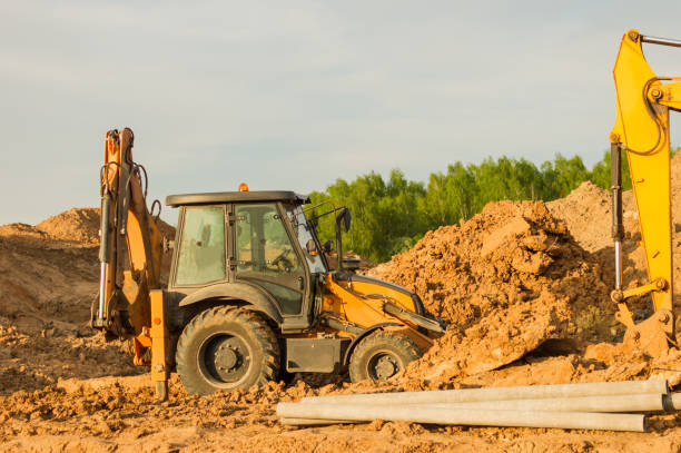 istock Yellow excavator during earthworks at construction site. Backhoe digging the ground for the foundation and for laying sewer pipes district heating. Earth-moving heavy equipment 1322476753