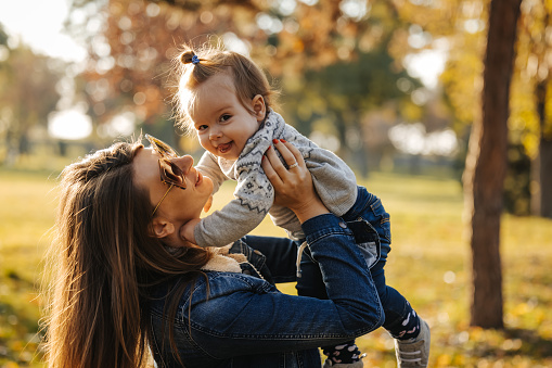 Happy young mother holding her smiling baby and enjoying sunny autumn afternoon in nature