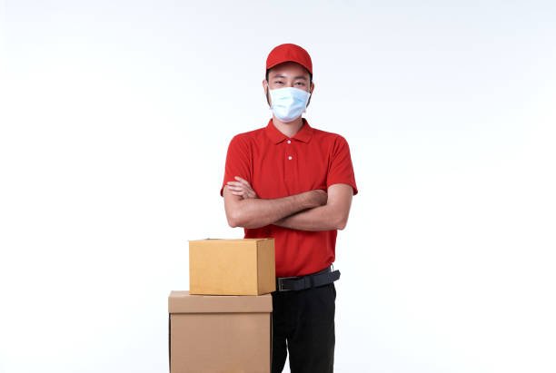 istock Asian delivery man wearing face mask in red uniform and parcel box isolated over white background. social distancing and new normal concept. 1322481643