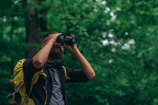 A hiker man walking in the forest using binoculars while looking for the bird that live in the nature