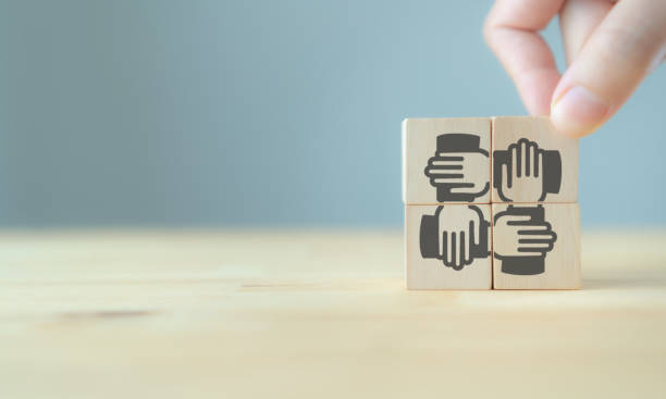 istock Hand pick up  wooden cube screening teamwork vector icon  standing on the wood table with blue background, copy space. Target for business management, teamwork, collaboration, achieve a common goal 1322485696