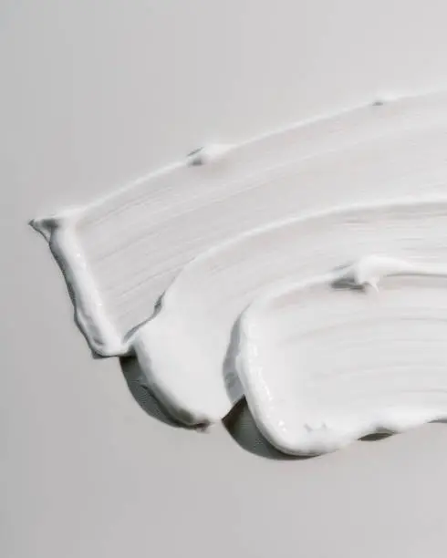 The texture of white cream on a white background on a round glass. Top view.