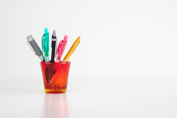 Different colorful pens in a red stained-glass cup isolated on white front view studio shot.