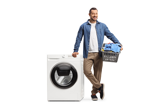 Casual young guy with a laundry basket and a washing machine isolated on white background