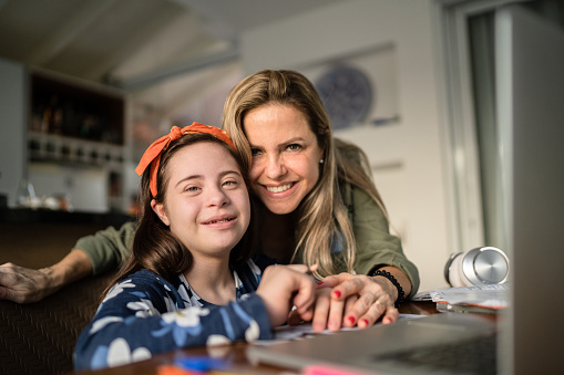 Portrait of mother and special needs daughter studying at home