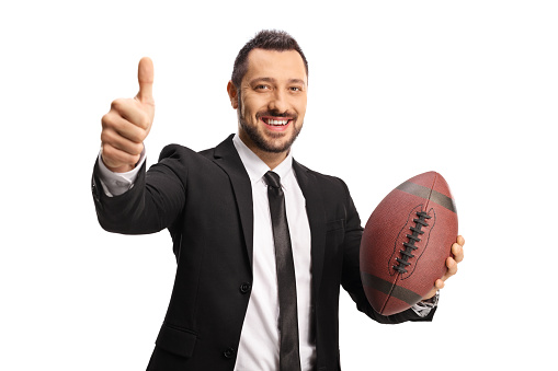 Smiling businessman holding a rugby ball and gesturing thumbs up isolated on white background