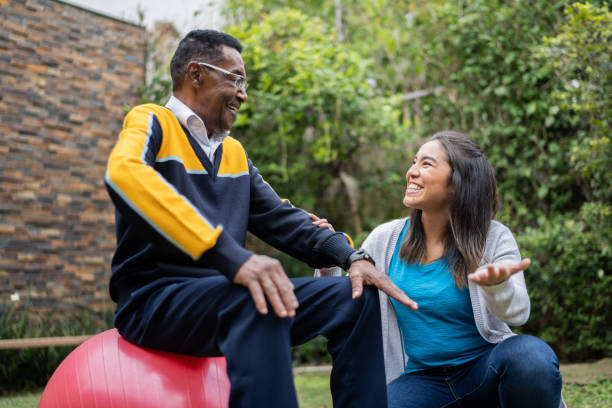 physiotherapeut im gespräch mit senior mann sitzt auf einem fitnessball zu hause - senior adult exercising aging process instructor stock-fotos und bilder