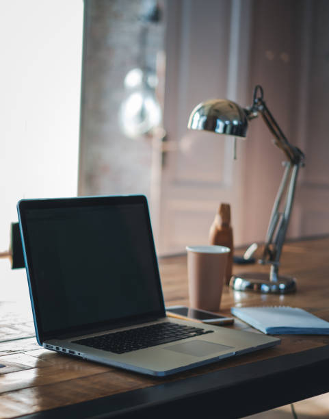 istock Computer laptop, notebooks and coffee cup on wooden desk in office with lamp, vertical image 1322498205