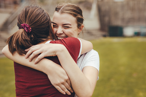 Two girls hugging each other in school campus. High school students smiling and embracing outdoors.