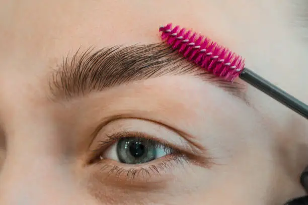 Photo of Combing, plucking eyebrows close-up. Close up of woman doing her make up, preparing brows using brush tool brushing eyebrows.