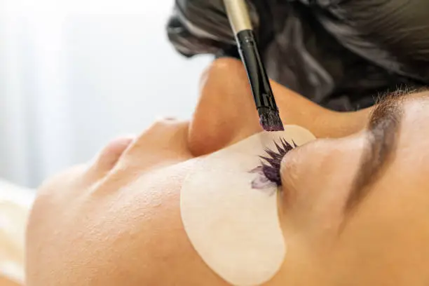 Eyelash care treatment procedures. Woman doing eyelashes lamination, staining, curling, laminating and extension for lashes. the master paints the client's eyelashes in a beauty salon. Closeup