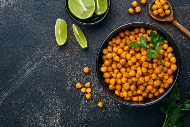 istock Fried chickpeas with turmeric with parsley and lime in black plate on an old black table background. Roasted spicy chickpeas or Indian chana or chole, popular snack recipe. Top view. 1322499615