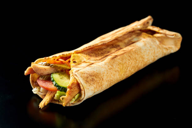 istock Appetizing shawarma with chicken, cucumbers, carrots and tomatoes in pita bread. Black background. Isolated. Close up, selective focus 1322500440