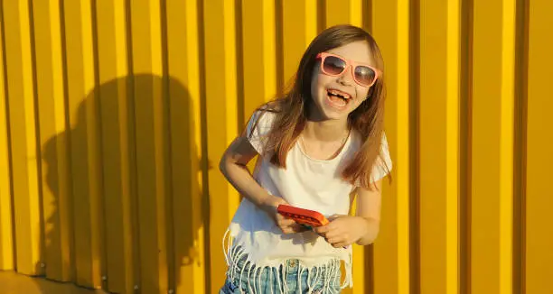 Photo of Smiling little girl holding a toy pop it on a yellow background