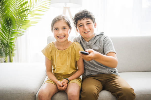 istock brother and sister sitting on the couch using a remote control 1322501814