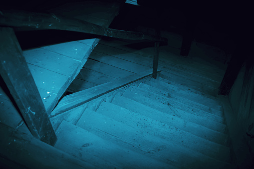 Mystical horror scary garret background to halloween. Old antique dirty wooden staircase in the dark in a mysterious paranormal spooky basement or attic with black shadow in the blue light of the moon