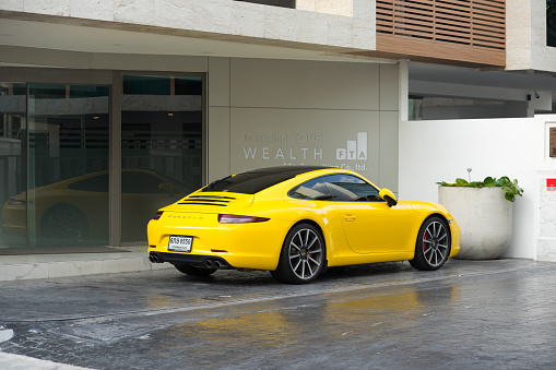 Yellow Porsche 911 parked in front of wealth management office building in Bangkok Ladprao in area of Ratchada 32