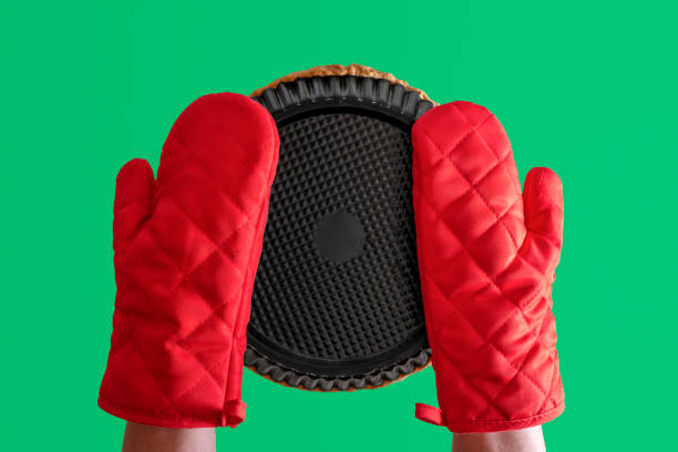 Woman hands protected with gloves taking out of oven baking tray. Holding baking tray with red gloves bottom-up view isolated on a green background.