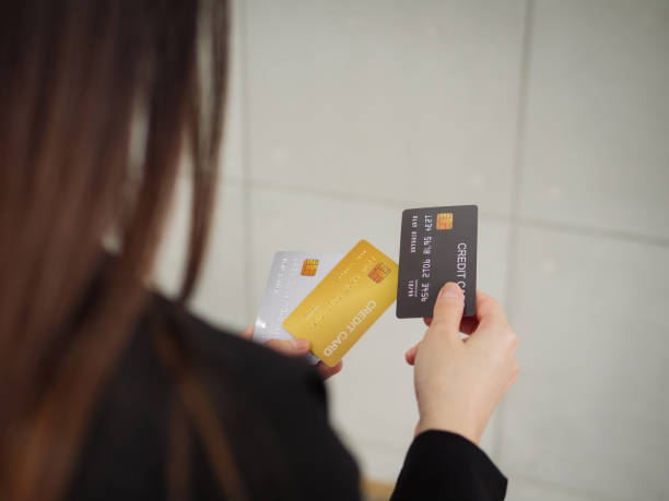 A rear view of a businesswoman in a black suit is holding three mockup credit cards in her hands. stock photo