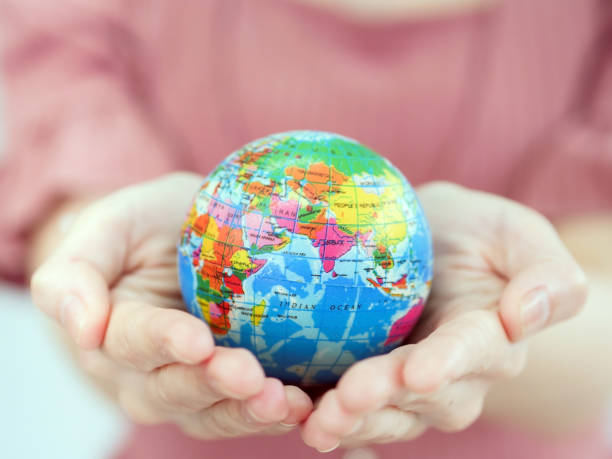 Close-up shot of hands of a female holding and showing a small globe protruding to the camera. stock photo