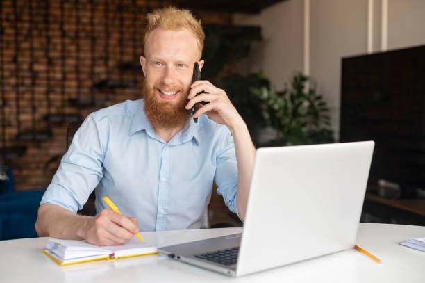 istock Intelligent and smart red haired man talking phone and work from home with laptop 1322515380