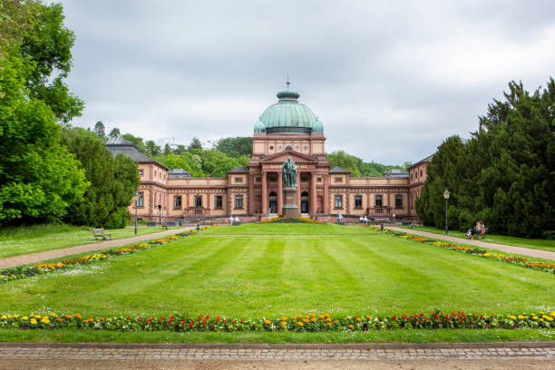 Bad Homburg, Germany - June 05, 2021: Facade of Kaiser-Wilhelms-Bad, Kurpark Bad Homburg, Germany. Some visitors and passersby in the foreground. The Kaiser-Wilhelm-Bad was built from 1887-1890, it is located in the spa park next to the famous casino and near the Elisabethenbrunnen. In front of the building the statue of Kaiser Wilhelm I.