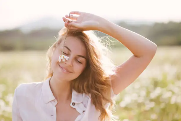 Young beautiful woman relaxing in chamomile field at sunset.