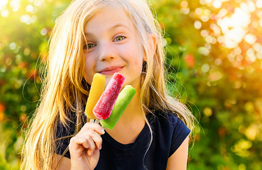 Cute and happy little girl with colorful frozen popsicles in the Summer nature background