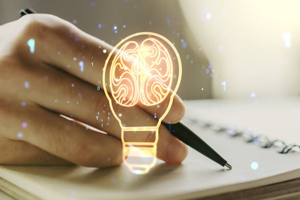 istock Creative light bulb with human brain hologram and with man hand writing in notepad on background, artificial Intelligence and neural networks concept. Multiexposure 1322520860