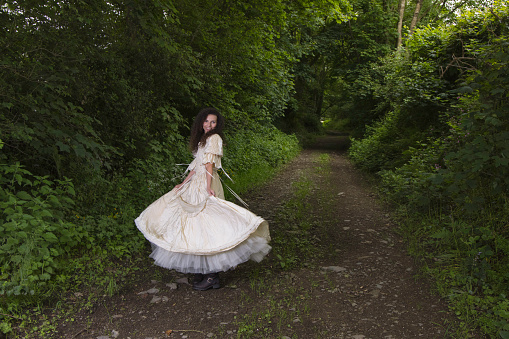 Dark-haired lady in a country lane twirling in her cream Victorian dress.