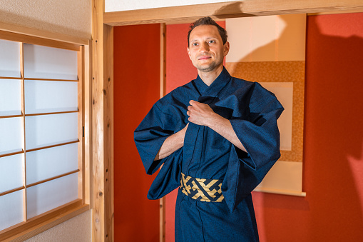 Traditional japanese machiya house room with sliding door window and red alcove with hanging scroll and happy man in blue kimono smiling at tea ceremony