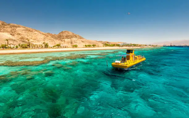 Nature with beautiful coral reefs of the Red Sea, pleasure boat, sandy beaches, tourist hotels and mountains near Eilat, Israel, Middle East