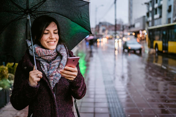 istock Woman using smartphone downtown in rain 1322537473