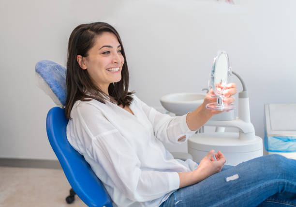 молодая женщина смотрит в зеркало с улыбкой в кабинете стоматолога - smiling dentist office dentists chair women стоковые фото и изображения