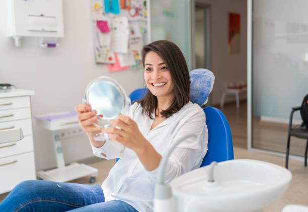 giovane donna che guarda specchio con il sorriso nell'ufficio del dentista - dentists chair immagine foto e immagini stock