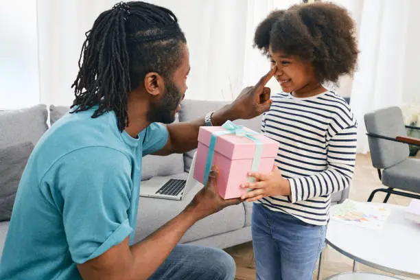Father gives a present to his daughter for her birthday. Happy African American female child with a surprise gift