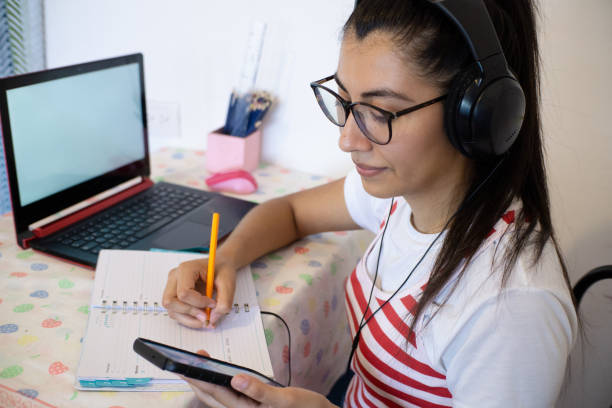 istock a Woman wearing headphones, using laptop, using cell phone, writing notes and smiling, online class concept, teaching online, internet business 1322544493