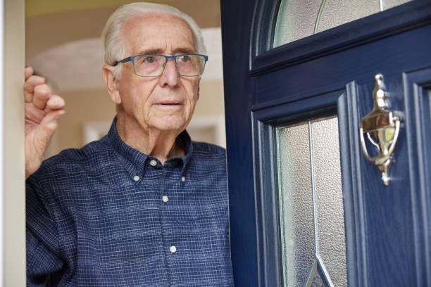 un homme âgé anxieux à la maison regardant par la porte d’entrée - porte dentrée photos et images de collection