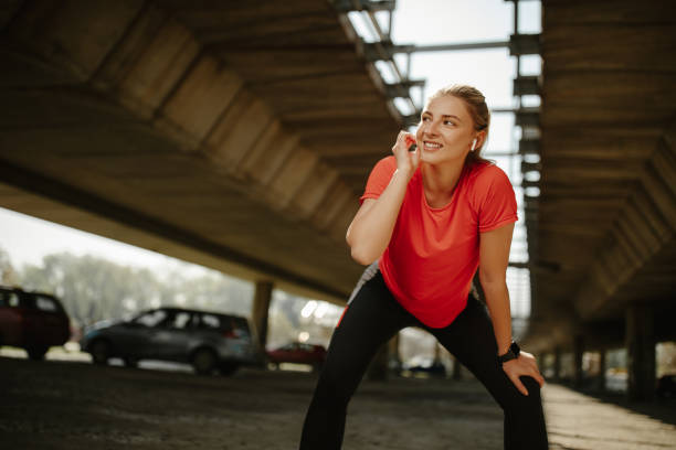 Runner taking break after jogging outdoors, looking away and listening a music on wireless earphones stock photo