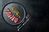 Juicy steak medium rare beef Filet Mignon or Eye Fillet, with onion and asparagus, on plate, with meat knife and fork, on black stone background, top view flat lay, with copy space for text