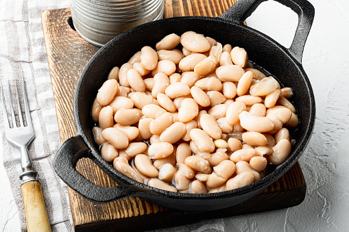 Canned white beans set, in cast iron frying pan, on white stone  surface