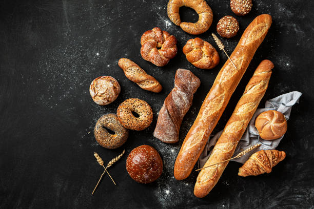 istock Breadstuff - bread rolls, baguette, bagel, burger bun and croissant on black background 1322559524