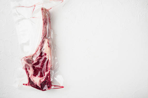 istock Tender raw trimmed bone-in ribeye tomahawk steak in pack, on white stone  background, top view flat lay, with copy space for text 1322561164