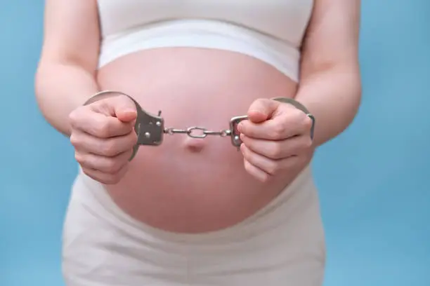Photo of Chained hands of a pregnant woman, studio shot on a blue background