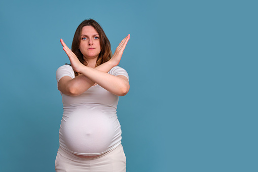 Pregnant woman refusal gesture, studio shot on blue background