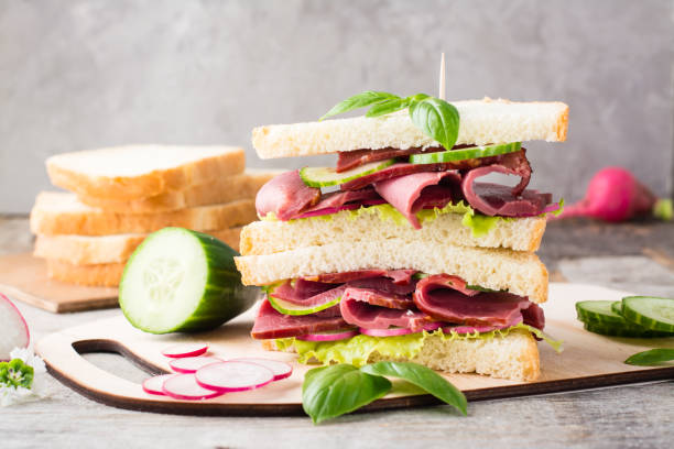 istock Double sandwich with pastrami, cucumber, radish and basil on a cutting board. American snack. Rustic style 1322562001