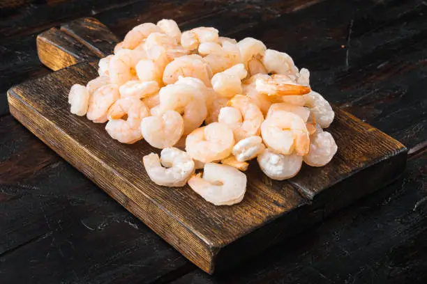 Photo of Boiled peeled shrimp prawns cooked, on wooden serving board, on old dark  wooden table